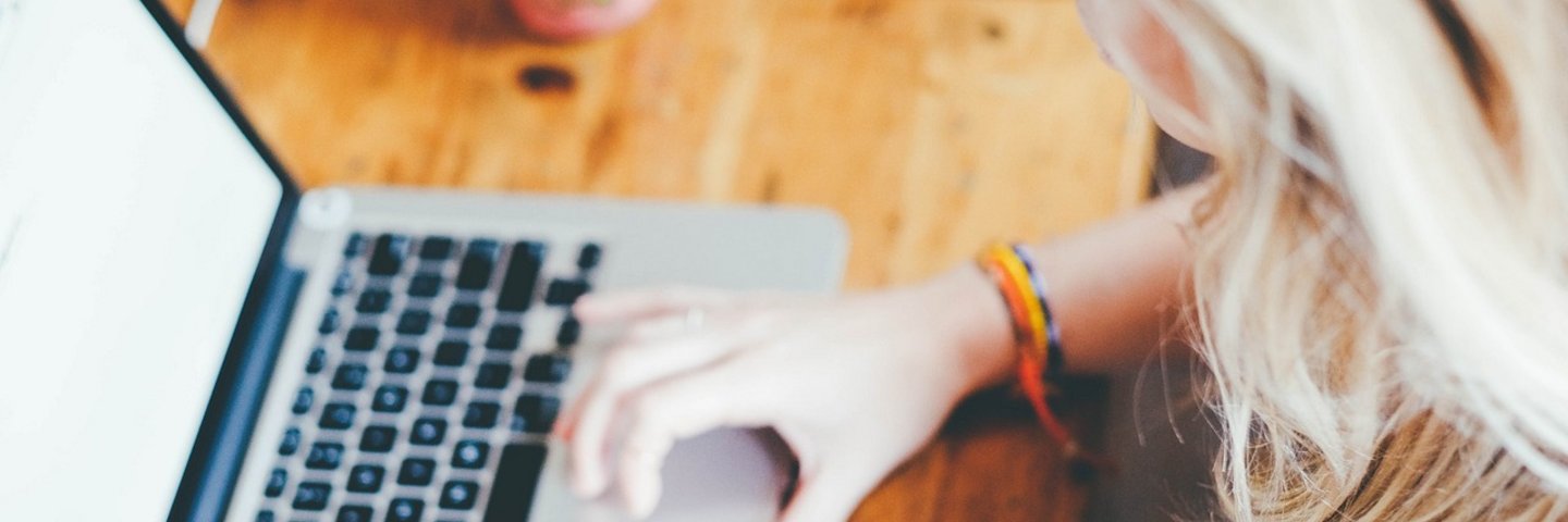 eine Person mit langen blonden Haaren arbeitet an einem Laptop
