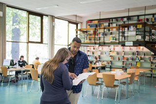 Zwei Personen schauen auf ein aufgeschlagenes Buch