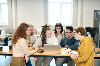 Ein Gruppe junger Leute sitzt zusammen um einen Laptop