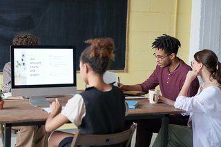 Junge Menschen sitzen in einem Klassenzimmer an Tischen vor dem Bildschirm